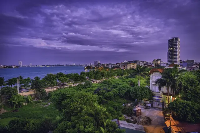 Hanoi lakeside at dusk, a high-rise above leafy streets by West Lake