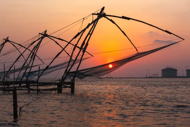 Cantilevered Chinese fishing nets silhouetted against an orange sunset at Fort Kochi
