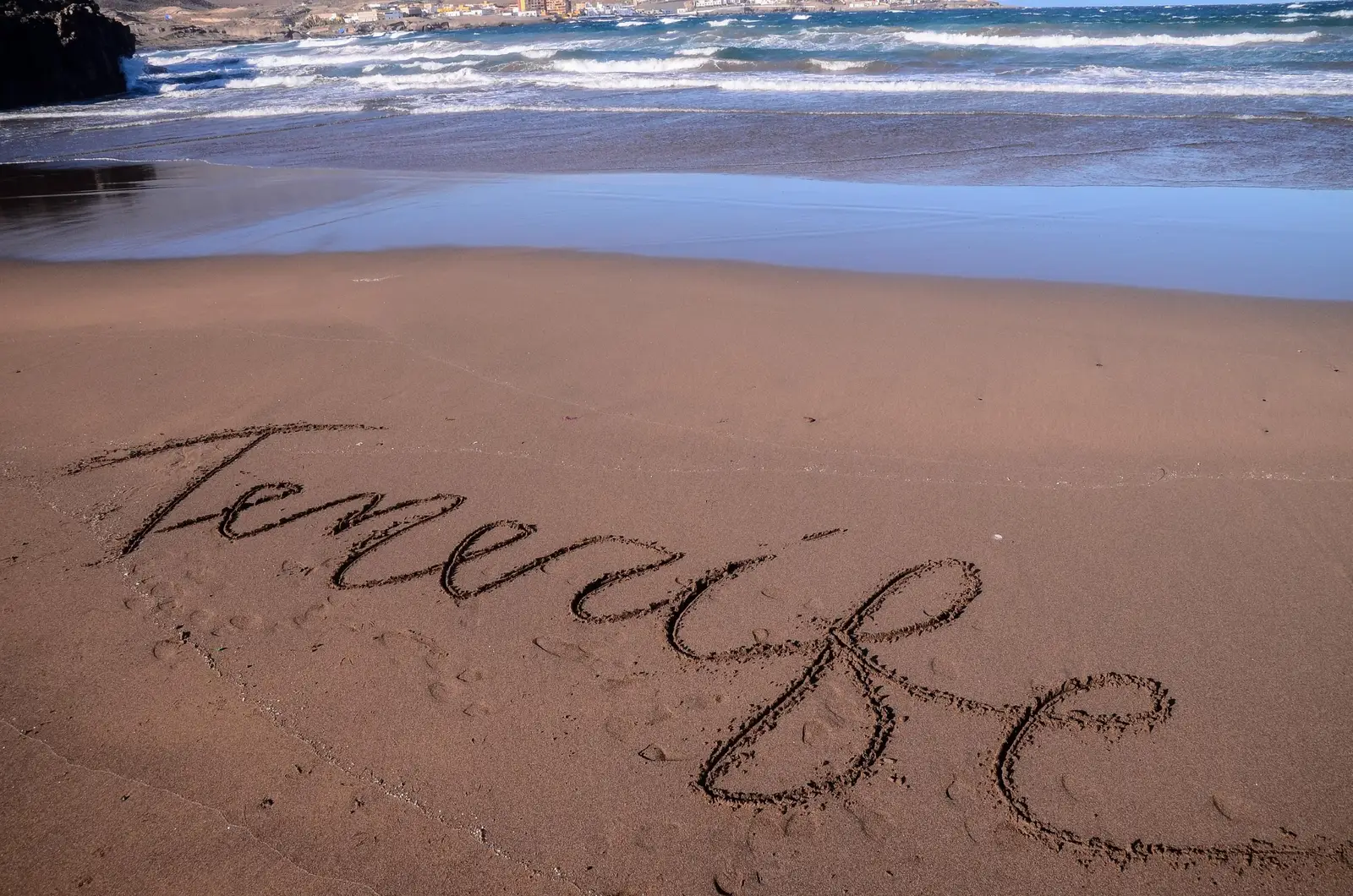 Tenerife written in the sand as waves roll in